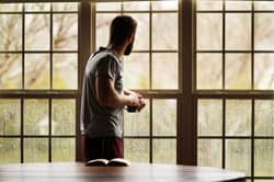 man in recovery looks out window with coffee and book