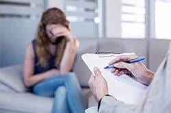 Woman sits with her head down as therapist writes notes