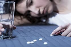 sad woman lying in bed looking at benzodiazepine pills